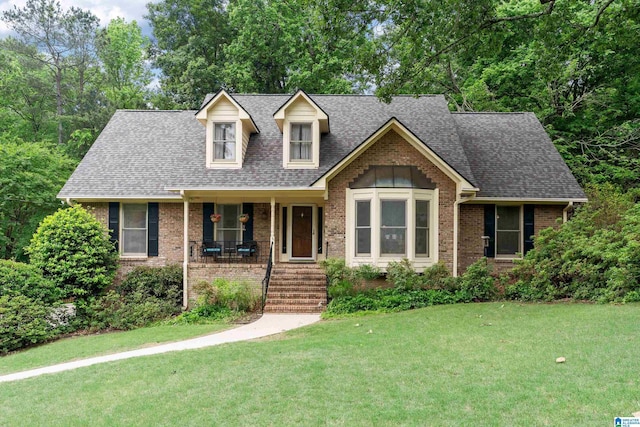 view of front of property featuring brick siding, a porch, a front yard, and roof with shingles