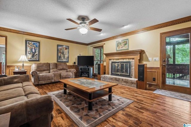 living area with wainscoting, ceiling fan, ornamental molding, a textured ceiling, and wood finished floors