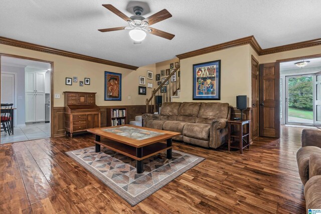living room featuring hardwood / wood-style floors, a ceiling fan, ornamental molding, a wainscoted wall, and a textured ceiling