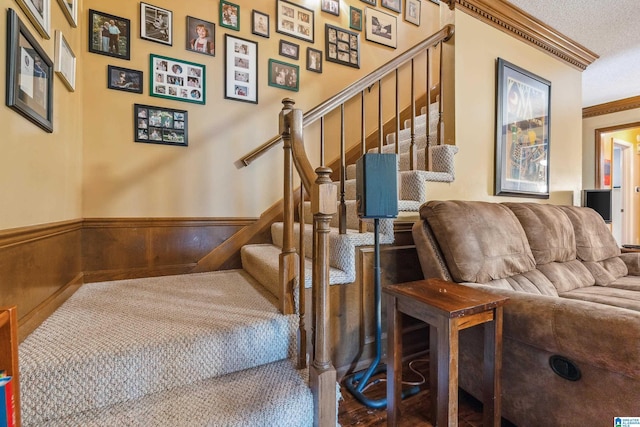 stairway with wainscoting, ornamental molding, and a textured ceiling