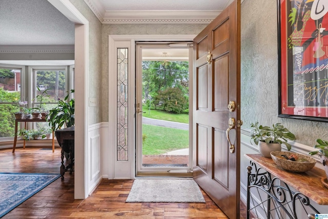 entrance foyer featuring wood finished floors, healthy amount of natural light, crown molding, a textured ceiling, and a wainscoted wall