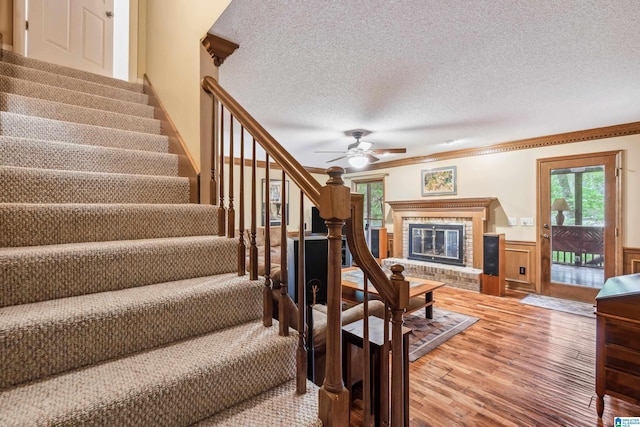 stairs featuring wood finished floors, a fireplace, a textured ceiling, a ceiling fan, and ornamental molding