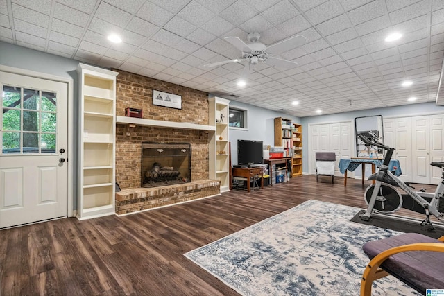 living room with wood finished floors, a brick fireplace, ceiling fan, and built in shelves