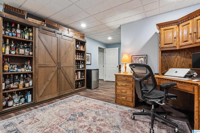 office area featuring wood finished floors, a drop ceiling, and a barn door