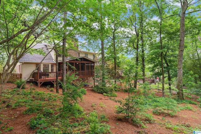 back of house featuring a sunroom, a wooden deck, roof with shingles, and fence