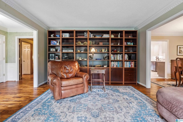living area with wood finished floors, ornamental molding, and a textured ceiling