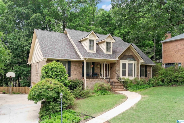 cape cod home with brick siding, a porch, a shingled roof, stairs, and view of scattered trees