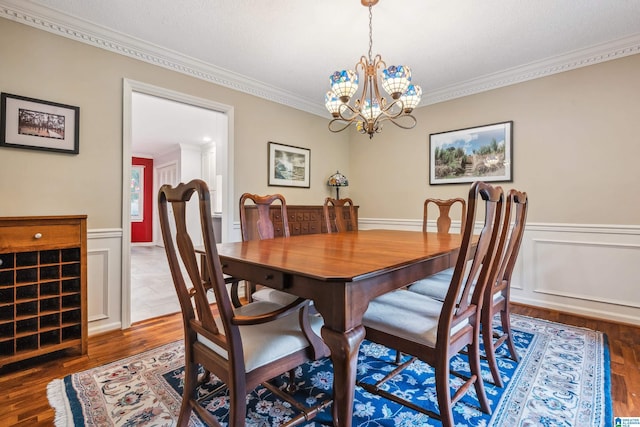 dining space featuring ornamental molding, a chandelier, wainscoting, and wood finished floors
