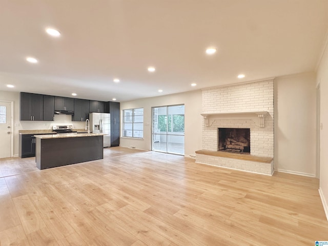 unfurnished living room featuring light wood-type flooring, recessed lighting, baseboards, a brick fireplace, and a sink