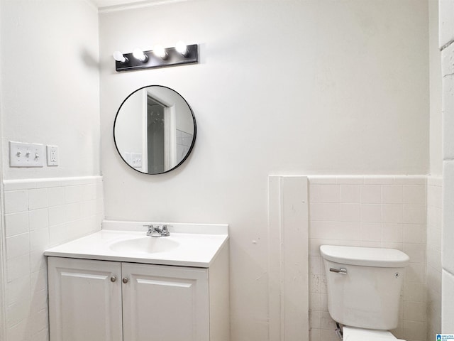 bathroom with tile walls, vanity, toilet, and a wainscoted wall