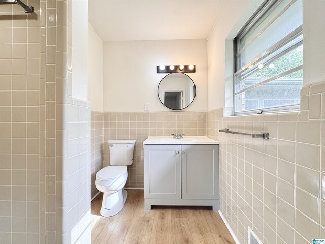 bathroom featuring tile walls, wood finished floors, toilet, wainscoting, and vanity