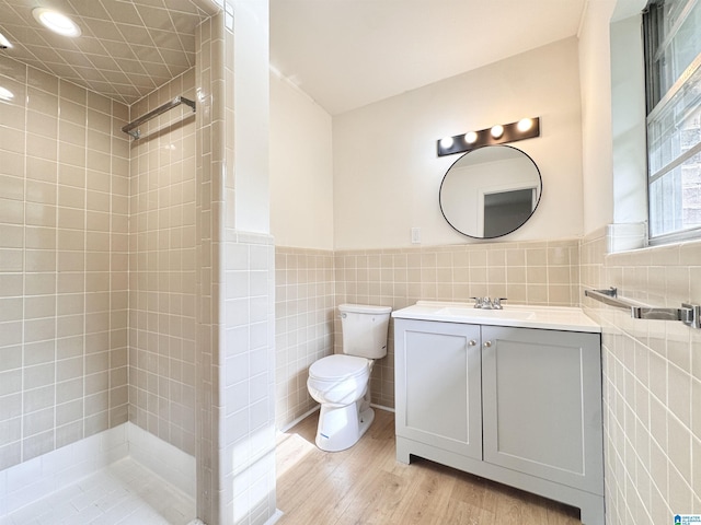 bathroom featuring tile walls, toilet, a tile shower, wood finished floors, and vanity