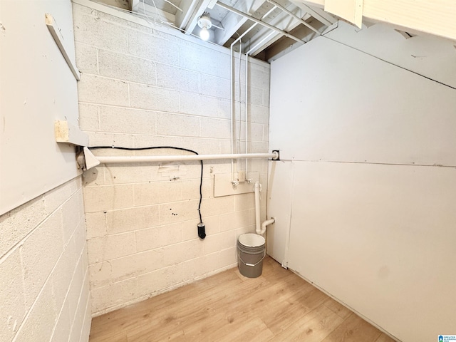clothes washing area featuring concrete block wall and light wood-style flooring