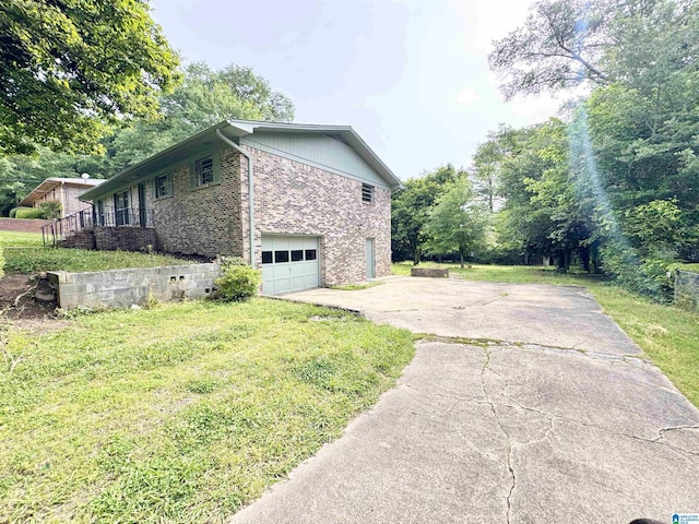 view of side of home featuring driveway, a garage, brick siding, and a yard