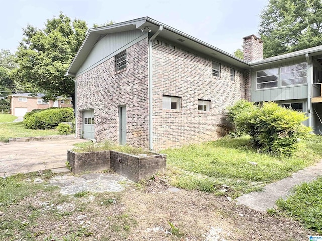 view of side of property with an attached garage, a chimney, driveway, and brick siding