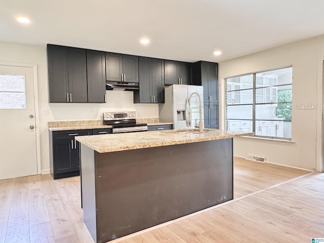 kitchen with stainless steel electric stove, under cabinet range hood, white refrigerator with ice dispenser, light wood finished floors, and a center island with sink