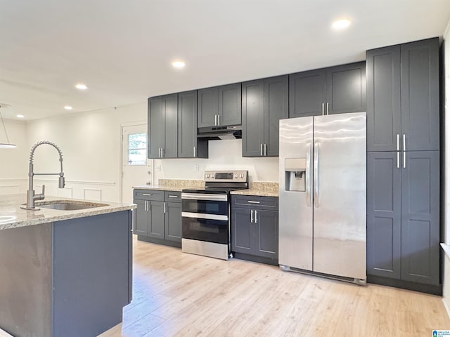 kitchen with stainless steel appliances, a sink, under cabinet range hood, light wood-style floors, and light stone countertops