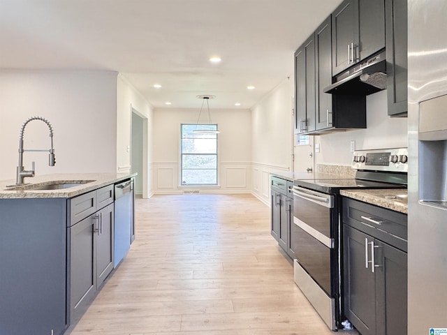 kitchen with appliances with stainless steel finishes, a sink, under cabinet range hood, light wood-style floors, and a decorative wall