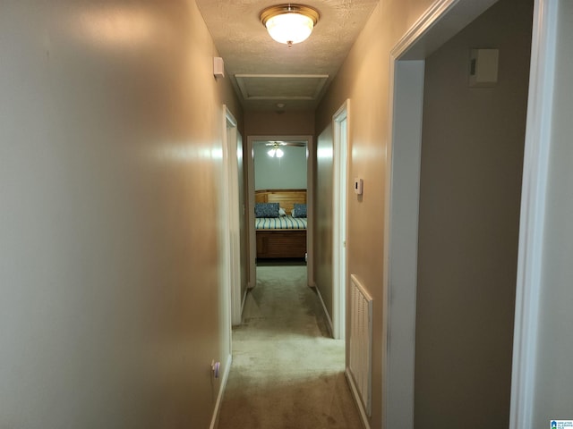 hallway featuring light carpet, attic access, and a textured ceiling