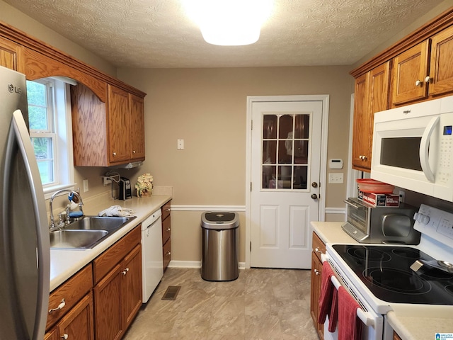 kitchen with white appliances, a sink, brown cabinetry, light countertops, and a textured ceiling