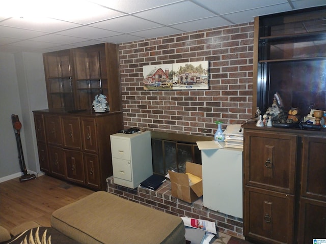 interior space with wood finished floors, baseboards, a paneled ceiling, and brick wall