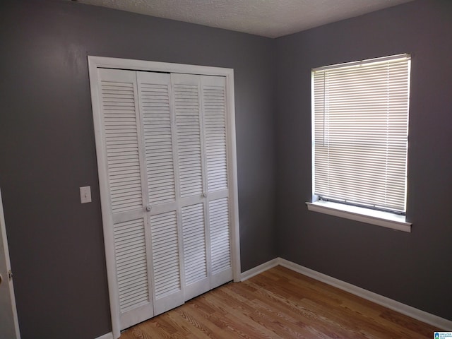 unfurnished bedroom featuring a closet, wood finished floors, baseboards, and a textured ceiling