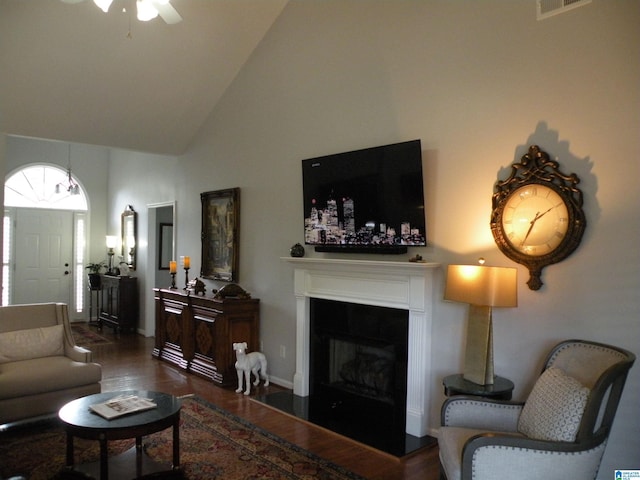 living area featuring high vaulted ceiling, wood finished floors, a glass covered fireplace, ceiling fan, and baseboards