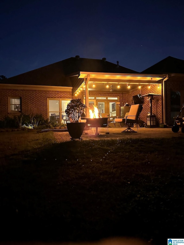 back of house at night with brick siding and a patio
