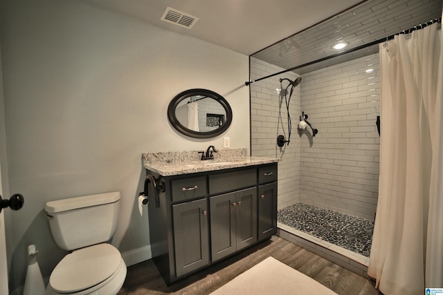 full bathroom featuring wood finished floors, toilet, tiled shower, vanity, and baseboards