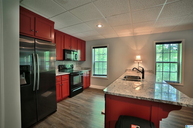 kitchen featuring black appliances, a sink, a peninsula, a drop ceiling, and a kitchen breakfast bar