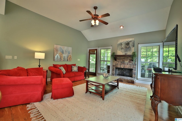 living area featuring wood finished floors, ceiling fan, a stone fireplace, lofted ceiling, and baseboards