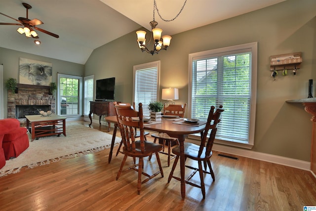 dining area featuring baseboards, a ceiling fan, wood finished floors, a stone fireplace, and a chandelier