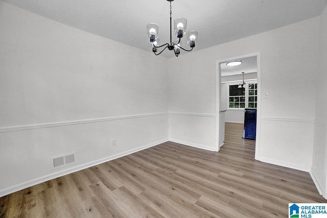 unfurnished dining area with a chandelier, wood finished floors, and baseboards