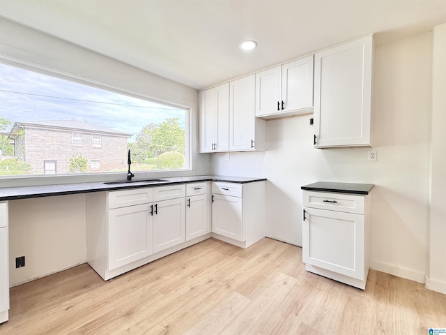 kitchen with a sink, light wood-type flooring, white cabinetry, dark countertops, and recessed lighting