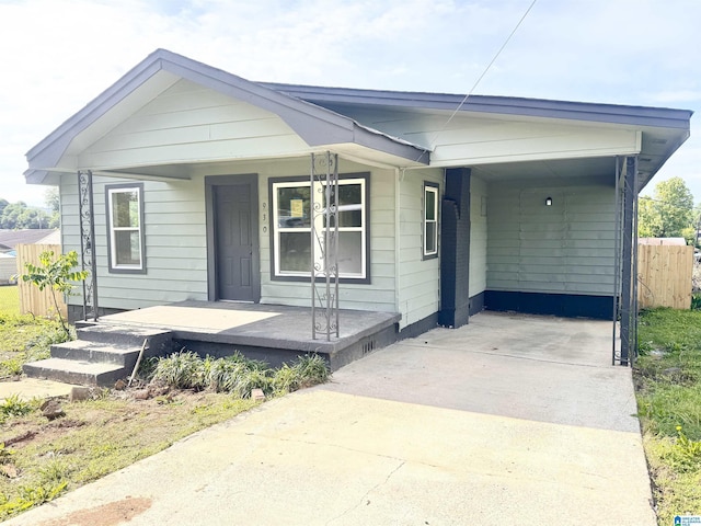 view of front facade with a porch, concrete driveway, a carport, and fence