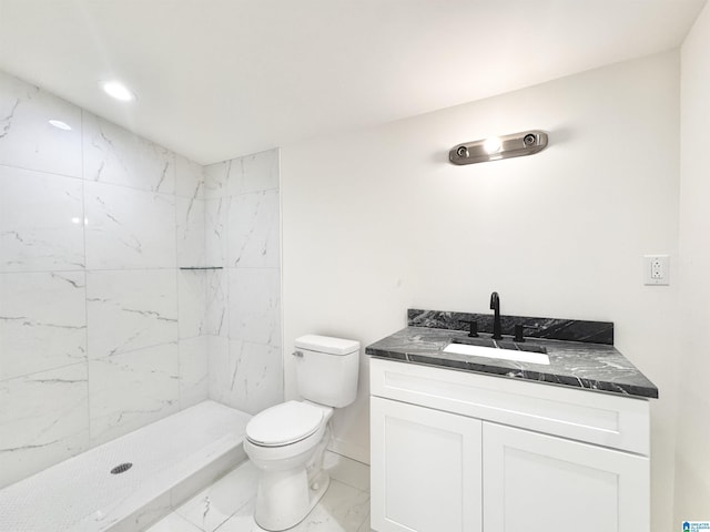 bathroom with marble look tiles, toilet, vanity, a tile shower, and baseboards