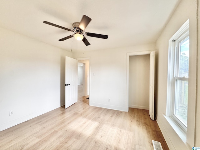 unfurnished bedroom featuring light wood-style floors, multiple windows, baseboards, and ceiling fan