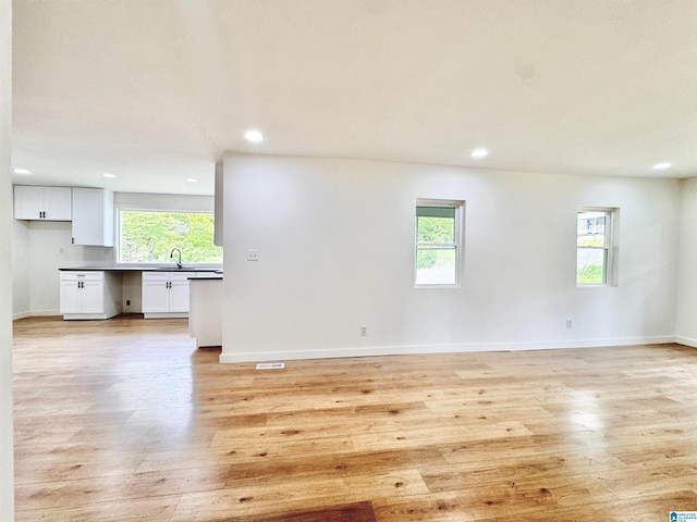 unfurnished living room featuring a sink, recessed lighting, light wood-style floors, and baseboards