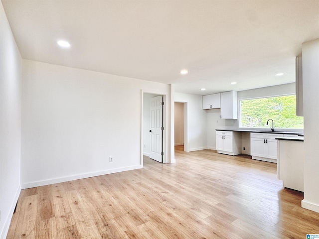 kitchen featuring white cabinetry, light wood-style flooring, a sink, recessed lighting, and dark countertops