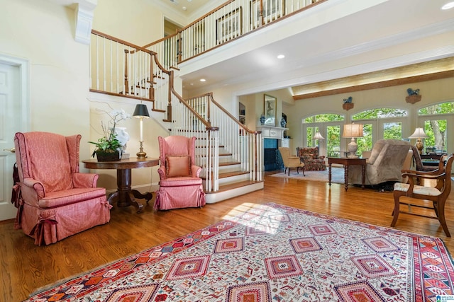living room with wood finished floors, stairway, ornamental molding, a high ceiling, and a fireplace