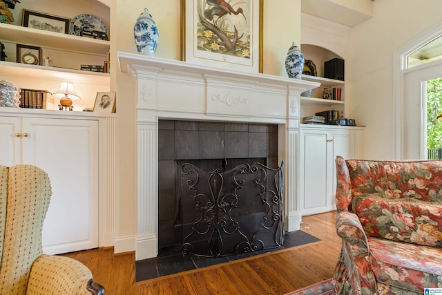 living area with a tile fireplace, wood finished floors, and built in shelves
