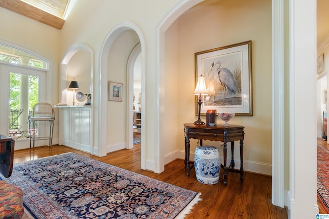 hallway with arched walkways, wood finished floors, and baseboards