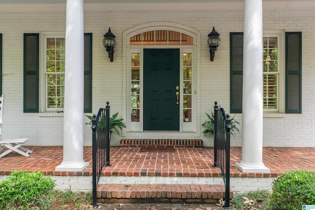 doorway to property featuring a porch and brick siding