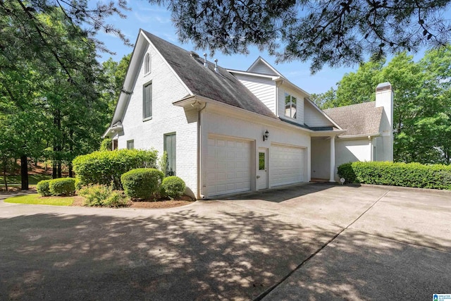 view of side of property with a chimney, concrete driveway, an attached garage, roof with shingles, and brick siding