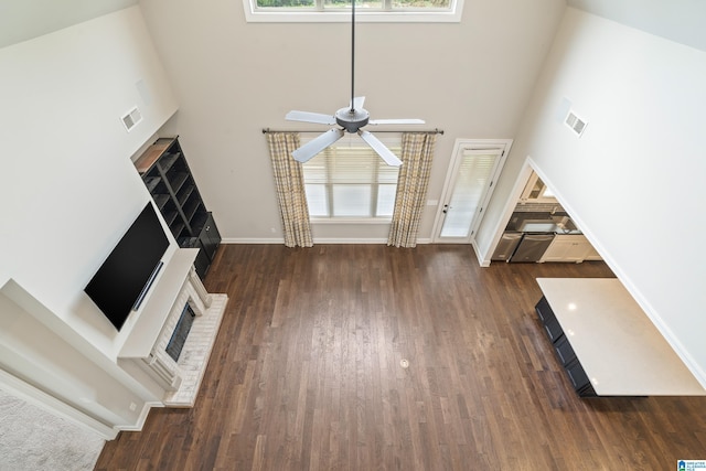 unfurnished living room featuring a high ceiling, a brick fireplace, a ceiling fan, dark wood-style floors, and baseboards