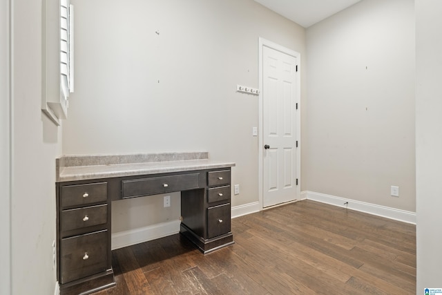 unfurnished office featuring built in desk, dark wood-style flooring, and baseboards