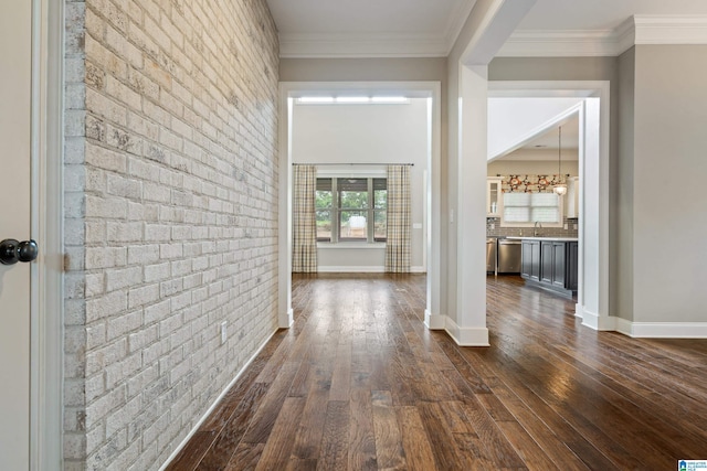 hall with dark wood finished floors, brick wall, crown molding, baseboards, and a sink