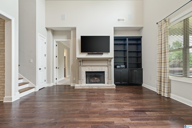 unfurnished living room with a towering ceiling, wood finished floors, a brick fireplace, baseboards, and stairs