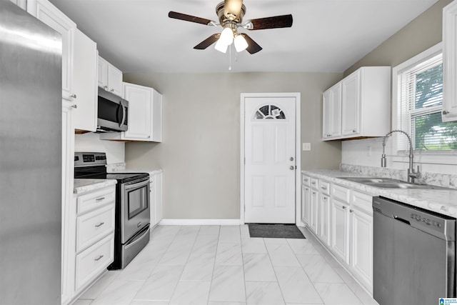 kitchen featuring appliances with stainless steel finishes, a sink, a ceiling fan, white cabinetry, and baseboards