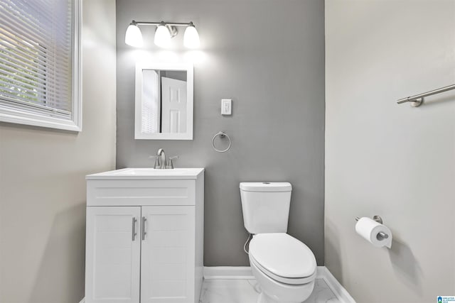 half bath with toilet, marble finish flooring, baseboards, and vanity